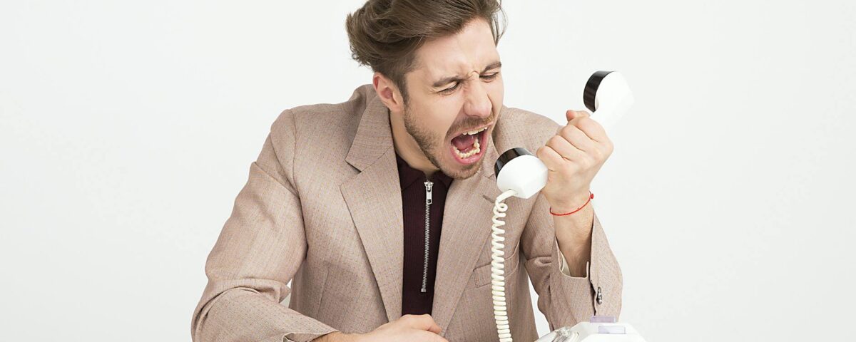 man wearing brown suit jacket mocking on white telephone