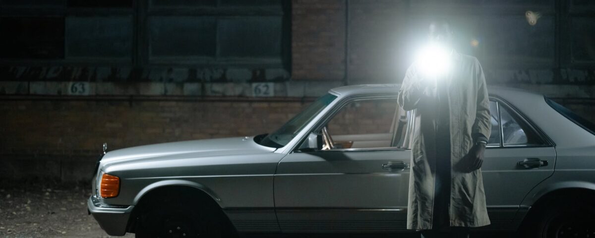 man in a trench standing beside the cat and holding a flashlight