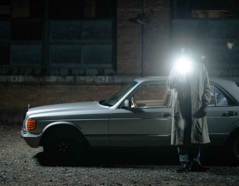 man in a trench standing beside the cat and holding a flashlight